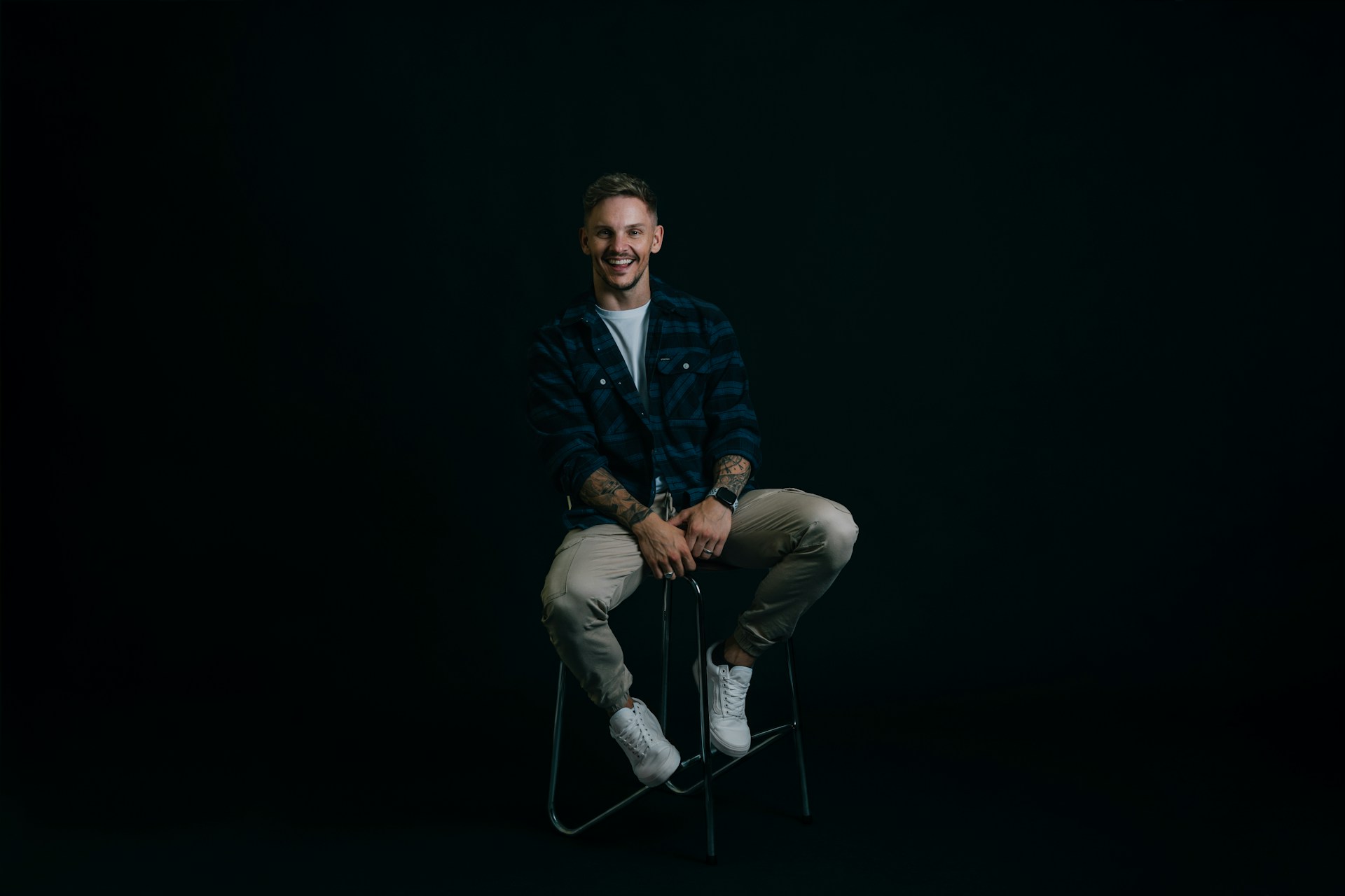 En manlig modell med stort leende, sittandes på stol i en fotostudio.