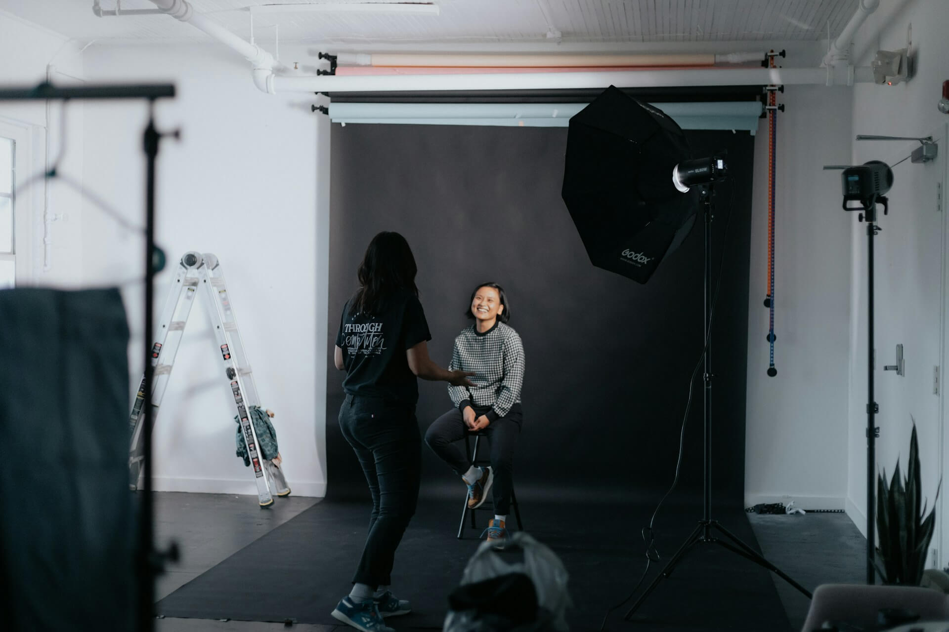 Vanliga frågor om fotografering stockholm. Kvinnlig modell som skrattar och blir stylad och rådgiven av annan fotograf.