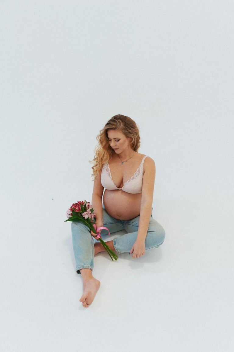 Gravid kvinna sittandes i en fotostudio med blombukett i handen.