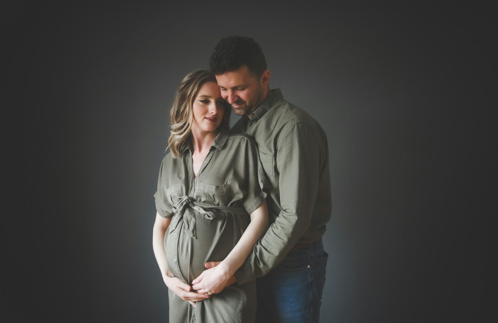 Ett gravid par som håller om varandra i en fotostudio.