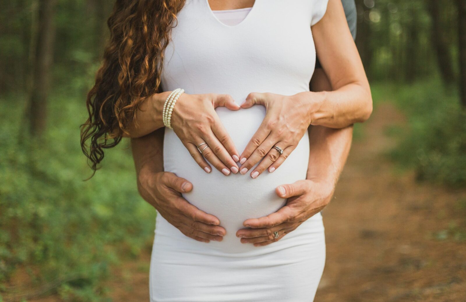 Gravidfotografering på man och kvinna som håller om och formar ett handhjärta över gravidmage.