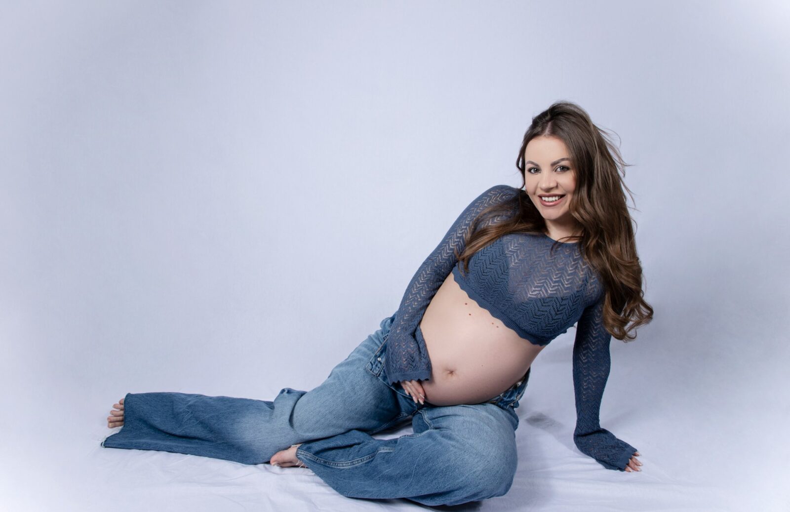 Kvinna som håller sin gravidmage, poserandes framför fotograf, i en studio under fotografering.