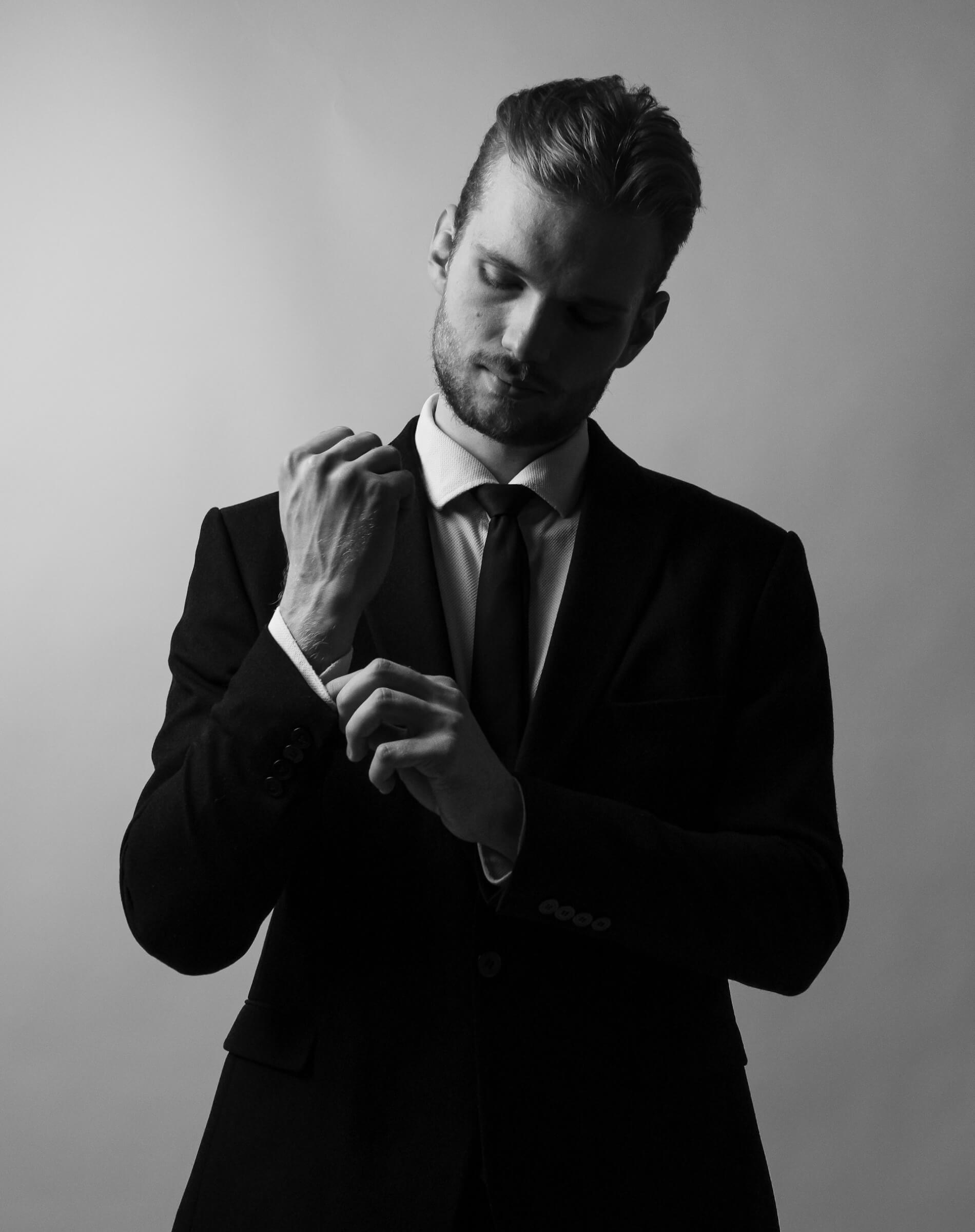 Svartvitt foto på man i kostym som rättar till ärmen på skjortan.